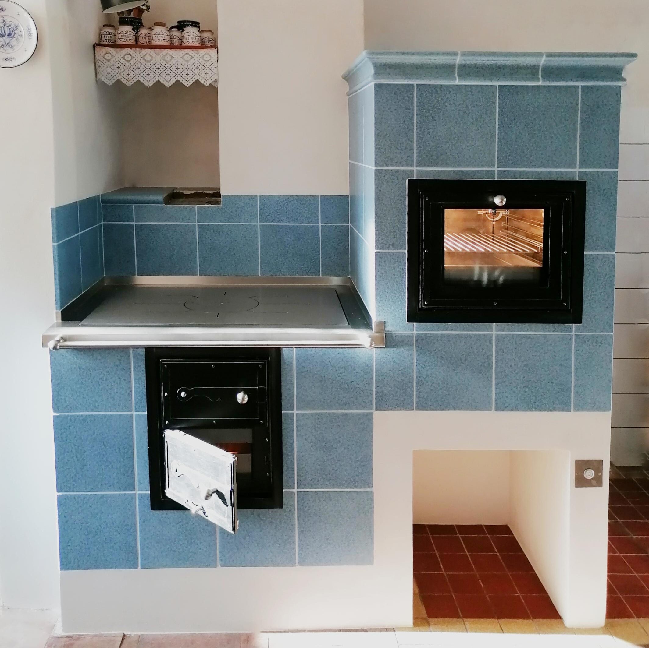 Kachlový sporák s kobkou v modré glazuře disponuje prosklenou troubou. Kování pochází od firmy Pertinger a je v rustikálním dekoru. Foto zdroj: Jihočeské kamnářství